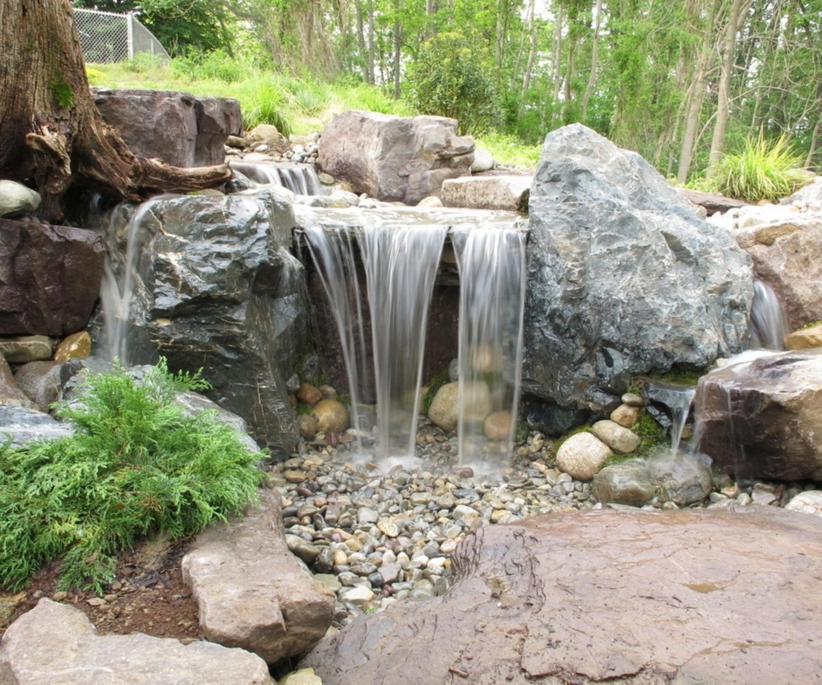 Natural boulder waterfall spilling into a planted pond