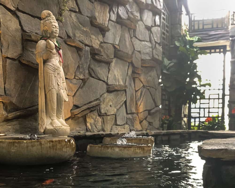 Stone statue beside bubbling bowl fountains in a courtyard pond