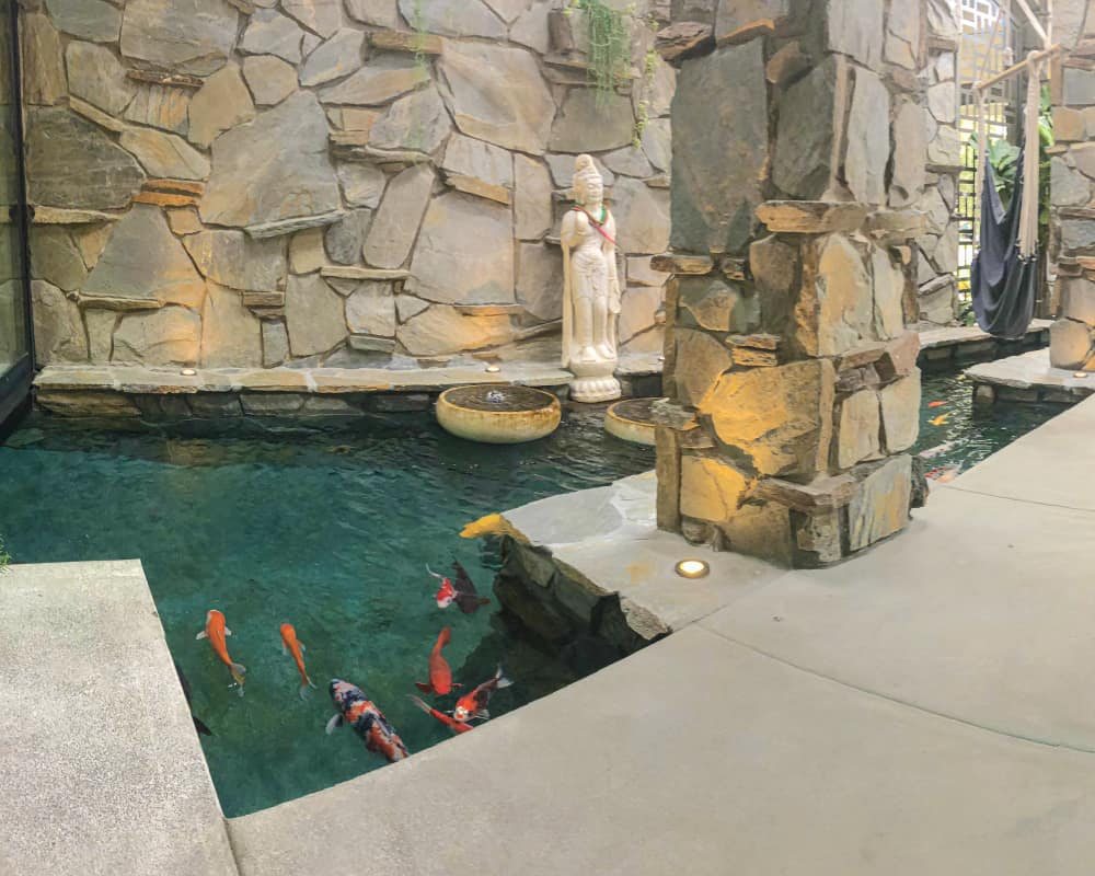 Wide view of a stone courtyard koi pond with statue, koi and pillar