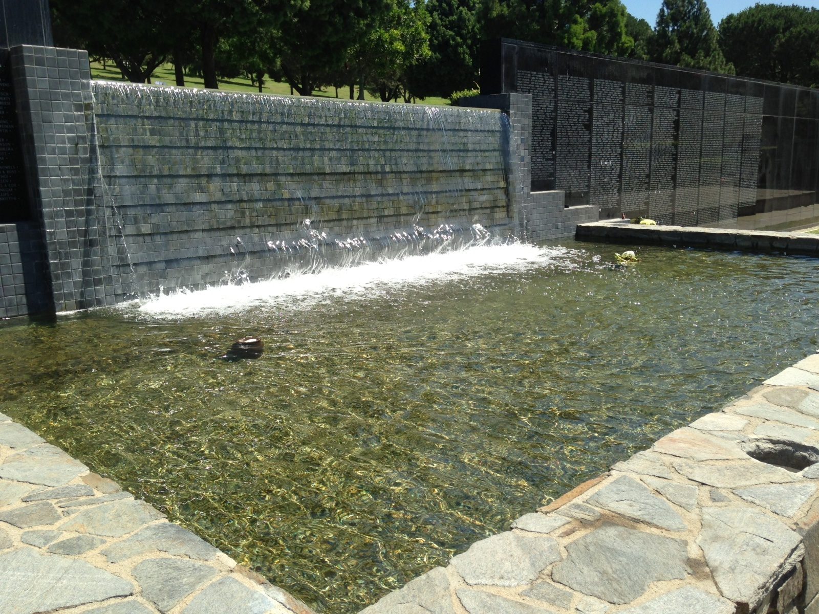 Tiled water wall spilling into a reflecting pool beside engraved memorial walls