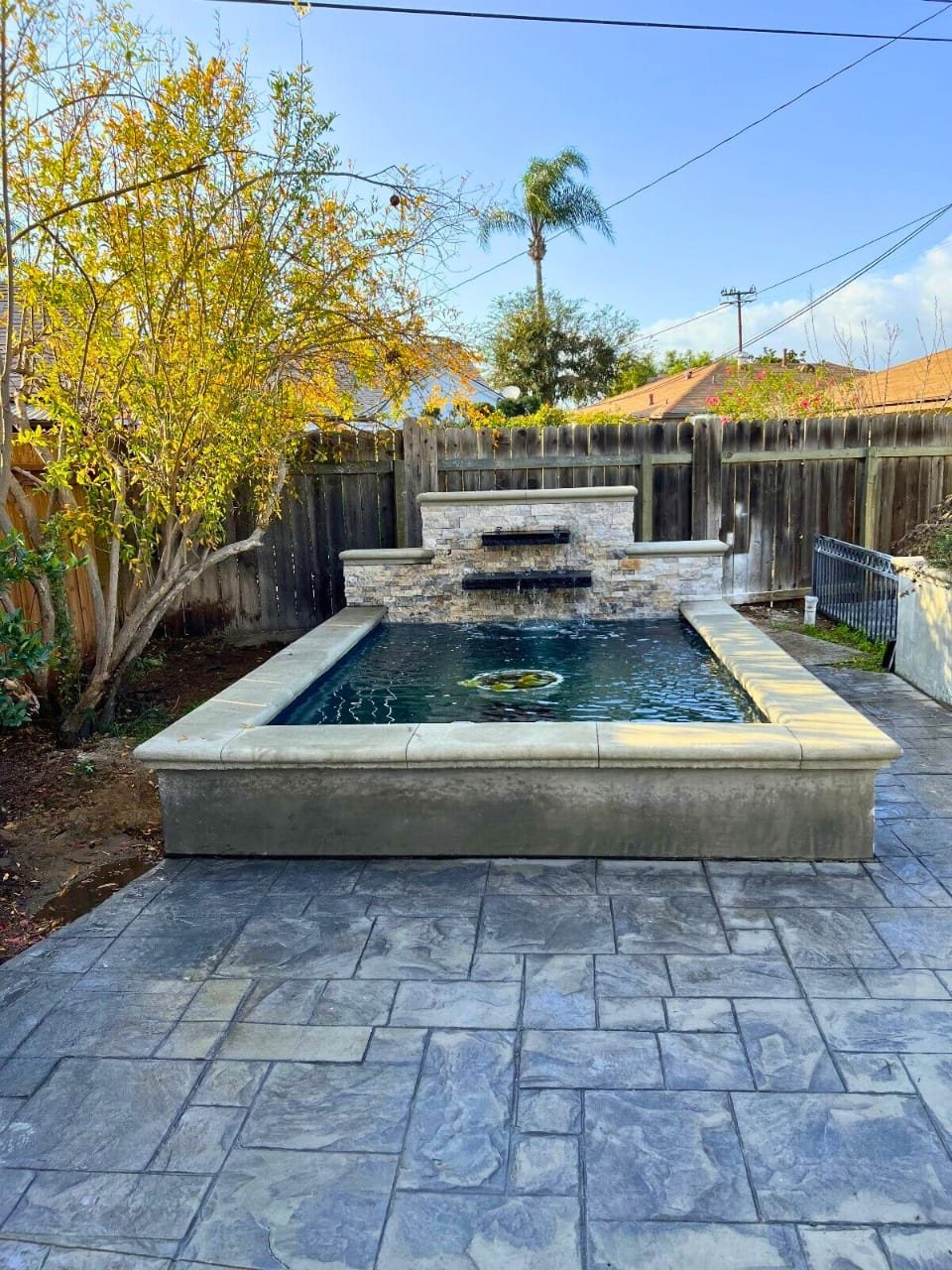 Raised formal koi pond with stacked-stone spillway wall and stamped concrete