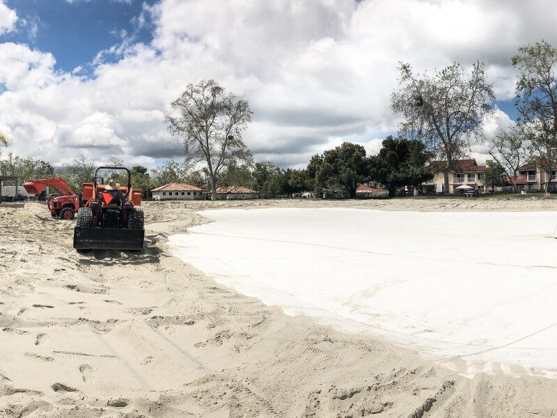 Tractor spreading sand over a new liner in a drained community lagoon, Rancho Santa Margarita