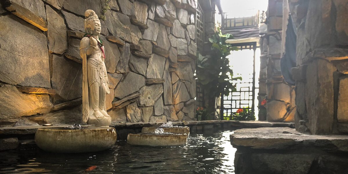 Stone grotto koi channel with statue and bubbling basins, lattice doors beyond