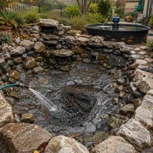 Waterfall and fountain in a garden pond with rocks and plants.