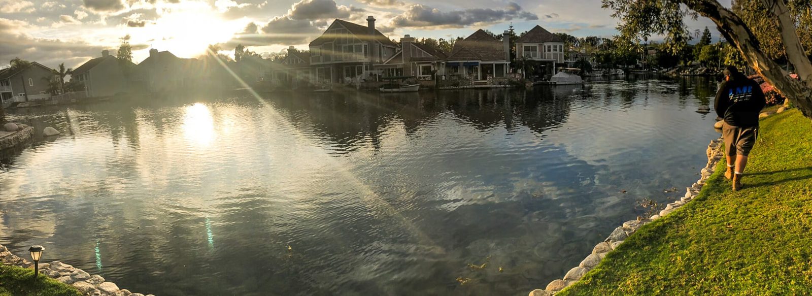 Koi Pros technician walking a stone-edged community lake at sunset
