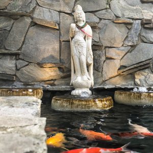 Stone statue over a courtyard koi pond with koi below