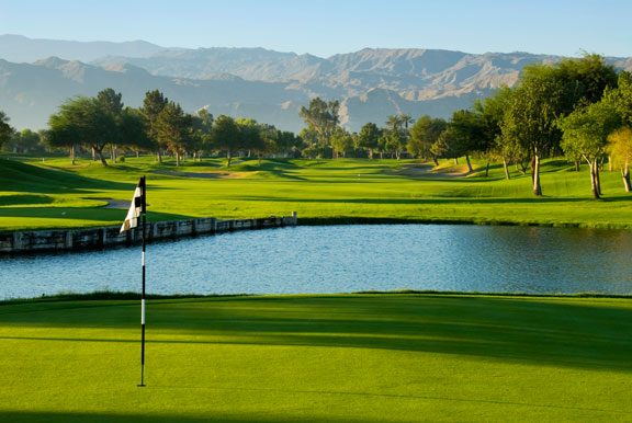 Desert golf green beside a lake with mountains behind