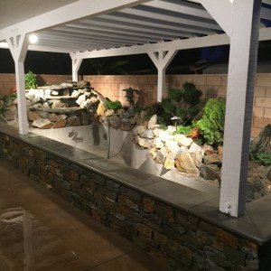 Raised koi pond with waterfall lit at night under a pergola, Garden Grove