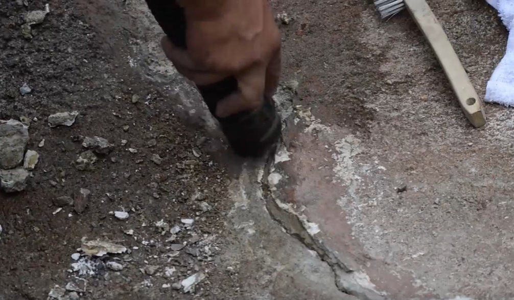 Technician grinding out a crack in a concrete pond shell before patching