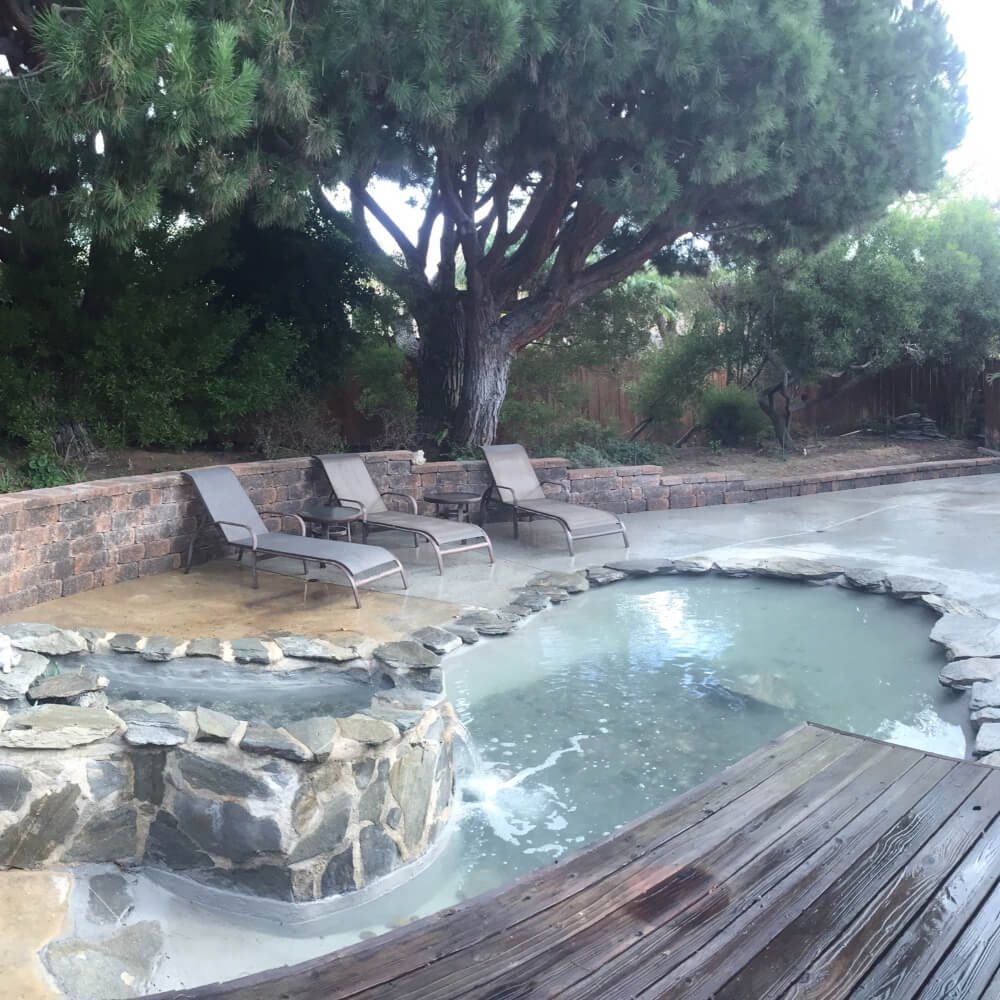 Natural rock spa pool with stone wall, lounge chairs and deck