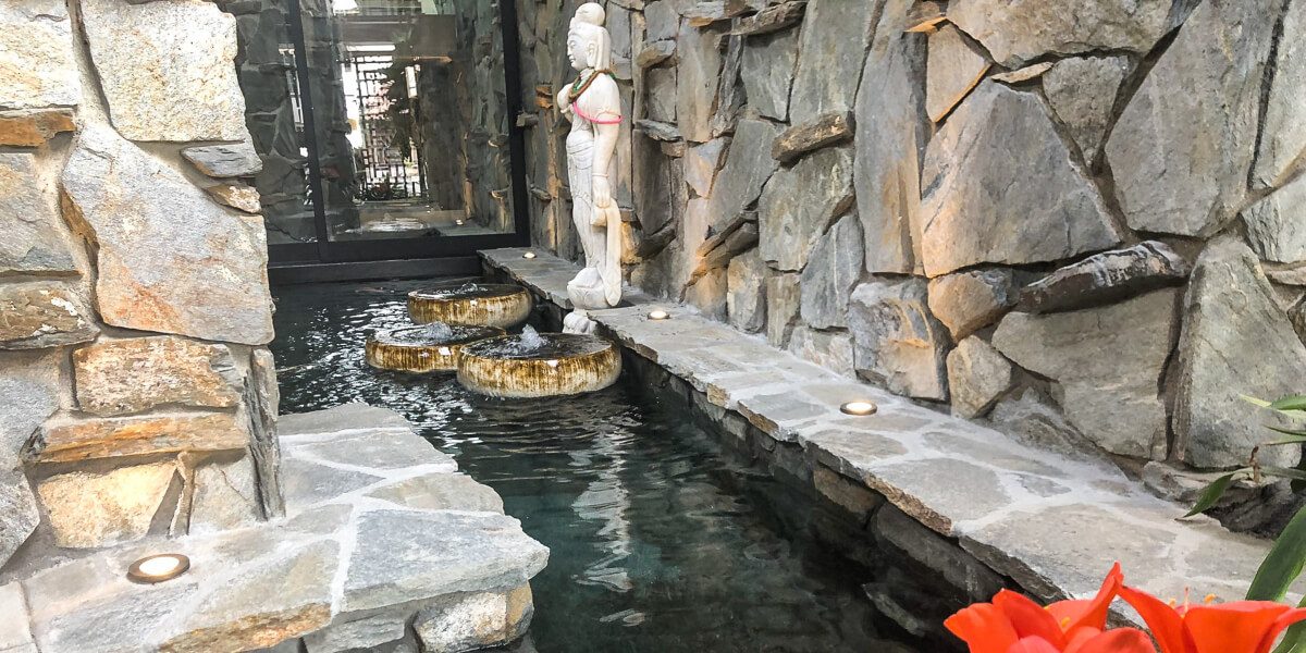 Stone-walled koi channel with three bubbling basins and a statue, glass walls beyond