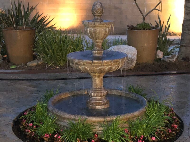 Three-tier cast-stone fountain ringed with begonias, lit at dusk