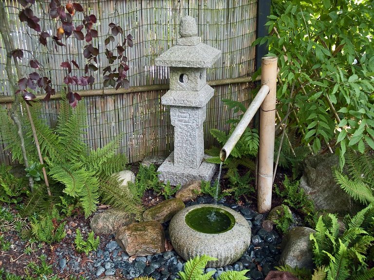 Bamboo spout feeding a stone basin beside a granite lantern
